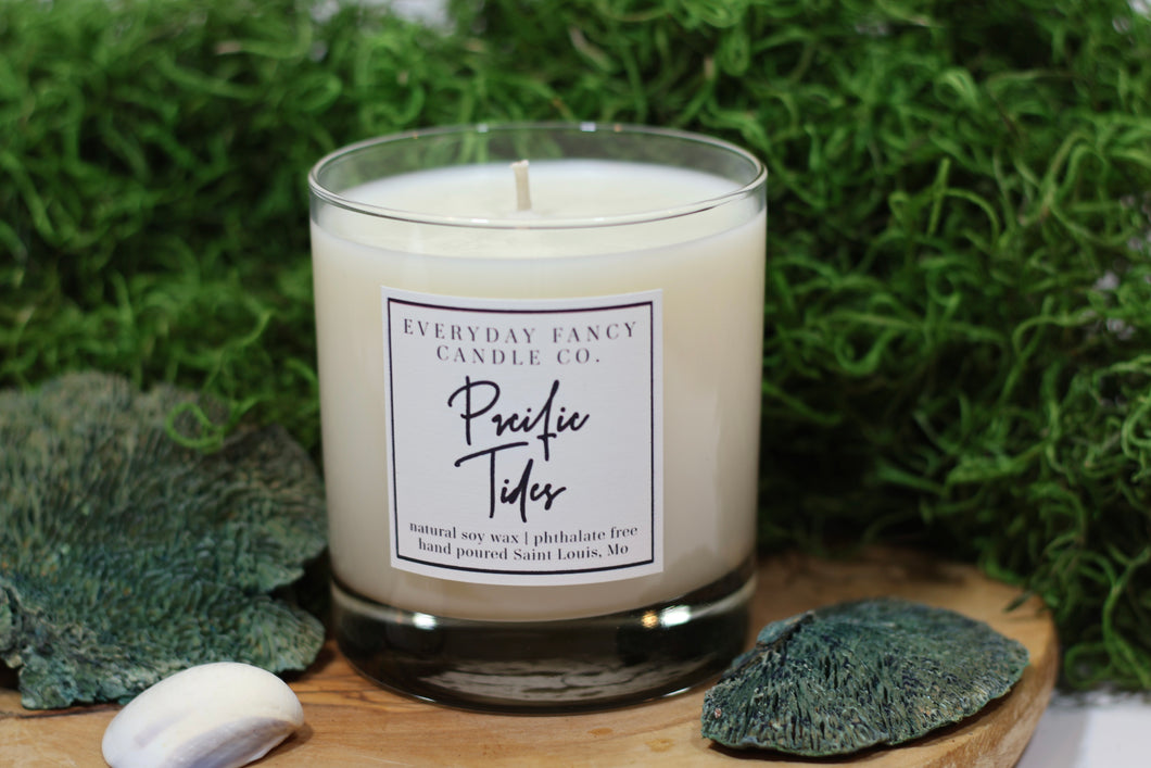 Soy Candle in a sleek glass jar. Simple classic label describes a scent with radiating fresh marine aromas accented by notes of honeydew and coconut. The fragrance evokes a serene coastal scene with turquoise waters and lush greenery