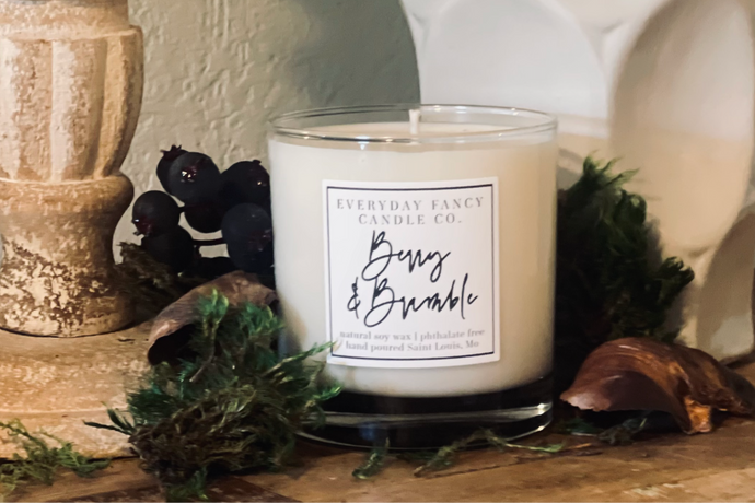 Candle with a label on a decorative surface with greenery and berries