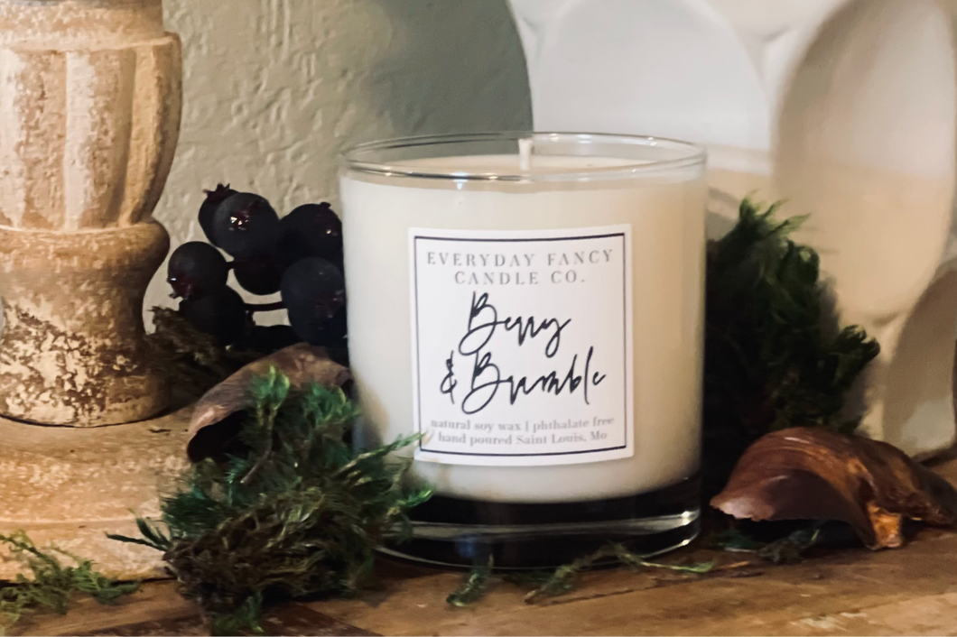 Candle with a label on a decorative surface with greenery and berries